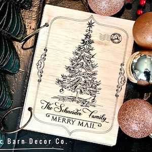 May include: A wooden Christmas card with a hand-drawn illustration of a Christmas tree and the text "The Schneider Family Merry Mail".