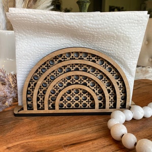 May include: A wooden napkin holder with a geometric design in the shape of a half circle. The holder is made of light brown wood and has a black base.