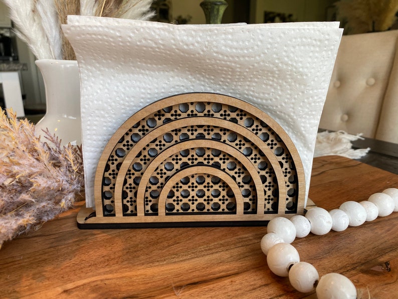 May include: A wooden napkin holder with a geometric design in the shape of a half circle. The holder is made of light brown wood and has a black base.