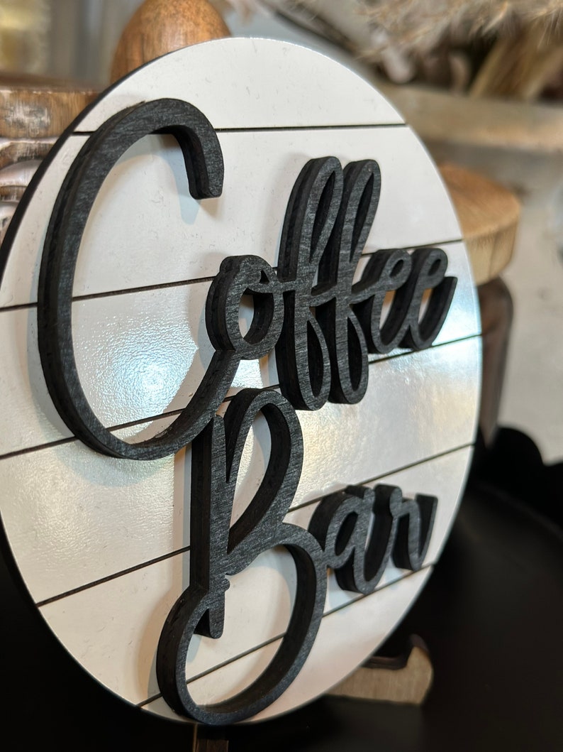 Pu&ograve; includere: Un cartello rotondo in legno con sfondo bianco e scritta nera che dice "Coffee Bar".