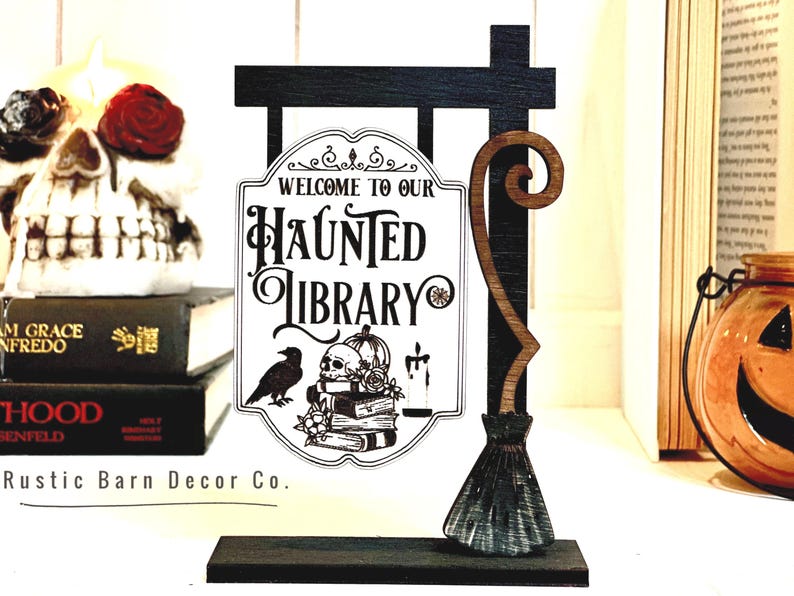 May include: A wooden sign with a black and white illustration of a haunted library. The sign is attached to a wooden post with a broom attached to the side. The sign reads "Welcome to our Haunted Library".