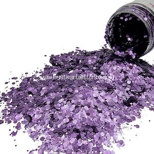 May include: A jar of purple glitter spills out onto a white background. The glitter is a mix of small and large hexagons, and it has a metallic sheen.