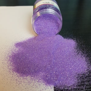 May include: A jar of purple glitter is spilling out onto a white surface. The jar is labelled "Purple Glitter".