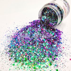 May include: A jar of iridescent glitter with a mix of green, blue, purple, and pink colours. The glitter is spilling out of the jar onto a white surface.