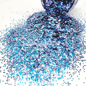 May include: A close-up of a pile of iridescent blue and pink glitter. The glitter is scattered on a white surface.