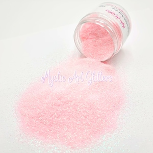 May include: A jar of pink glitter with iridescent shimmer. The glitter is spilling out of the jar onto a white surface. The jar has a label that says "Mystic Art Glitters" and "White Rose Pink".