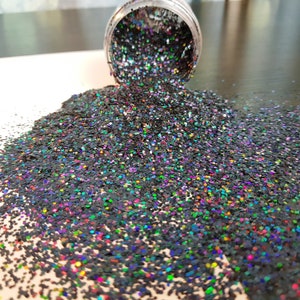 May include: Black glitter with iridescent rainbow flecks. The glitter is loose and spilling out of a clear jar.