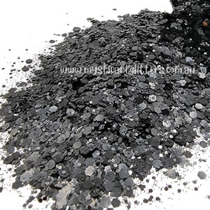 May include: A close-up of black and silver glitter, with a variety of sizes and shapes. The glitter is piled high, creating a textured surface. The website address "www.mysticalglitter.com.au" is visible in the image.
