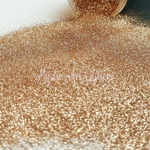 May include: A close-up shot of a pile of fine, shimmering gold glitter. The glitter is spilling from a small container, creating a textured surface. The text "Mystic Art Glitters" is visible in the image.
