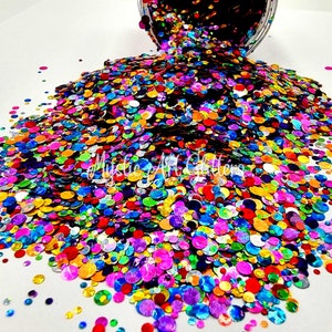 May include: A large pile of colourful iridescent glitter in various sizes. The glitter is in the shape of circles and is scattered on a white surface. The glitter is a mix of colours, including red, orange, yellow, green, blue, purple, and silver.