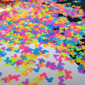 May include: A scattering of colourful Mickey Mouse head shaped glitter. The glitter is in shades of pink, blue, yellow, green, and orange.