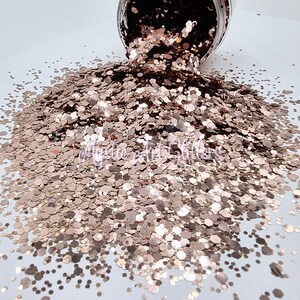 May include: A close-up of a pile of rose gold glitter. The glitter is a mix of different sizes and shapes, and it is very sparkly.