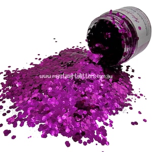 May include: A jar of bright purple glitter is shown, with a large quantity of hexagonal glitter spilling out. The glitter is a deep magenta hue, reflecting light. The website address "mysticartglitters.com.au" is visible on the spilled glitter.