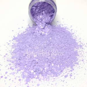 May include: A jar of light purple glitter with a holographic finish. The glitter is spilling out of the jar onto a white surface. The glitter is labelled "Mystic Art Glitters".