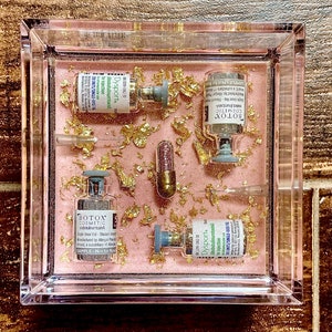 May include: A clear acrylic box filled with gold flakes and pink resin, containing four vials of Dysport and Botox cosmetic injectables. The vials are labeled with the product name, dosage, and instructions for use.