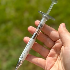 May include: A white and silver syringe with the text "Rejuve Health Plus" printed on the side.