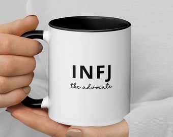 May include: White ceramic mug with a black rim and handle. The mug has black text that reads "INFJ the advocate".