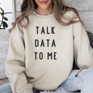 Pode incluir: Uma camisa de moletom bege com o texto "TALK DATA TO ME" impresso em preto.