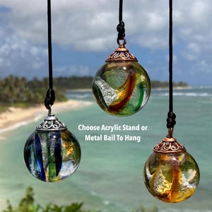 Pode incluir: Tr&ecirc;s pingentes de globo de vidro com designs internos coloridos, suspensos por cord&otilde;es pretos. Os globos t&ecirc;m tampas de metal e s&atilde;o exibidos em um cen&aacute;rio de praia. O texto diz "Choose Acrylic Stand or Metal Bail To Hang."