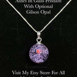 Pode incluir: Colar de prata com um pingente redondo de vidro transparente, com interior roxo e branco e uma opala Gilson vermelha. O texto na imagem diz: "Ashes In Glass Pendant With Optional Gilson Opal".