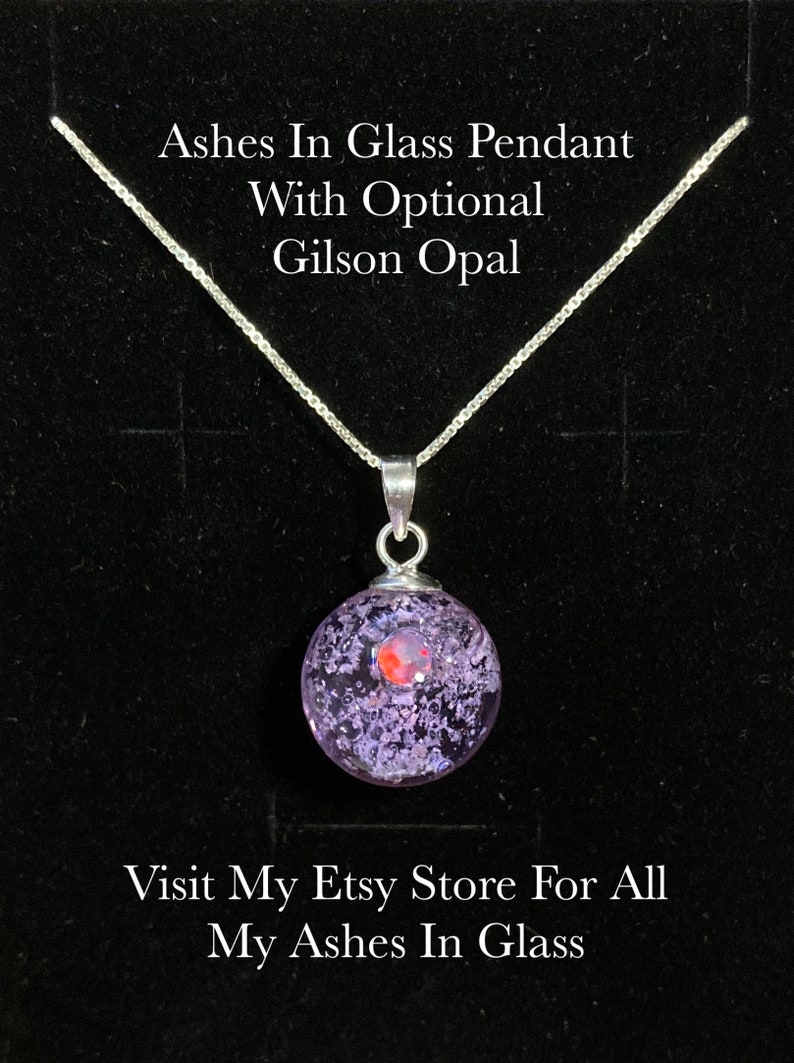 Pode incluir: Colar de prata com um pingente redondo de vidro transparente, com interior roxo e branco e uma opala Gilson vermelha. O texto na imagem diz: "Ashes In Glass Pendant With Optional Gilson Opal".