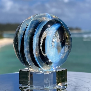 May include: A glass paperweight with swirling blue and black patterns on a clear glass base.
