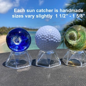 Pode incluir: Tr&ecirc;s apanhadores de sol feitos &agrave; m&atilde;o em suportes transparentes. Os apanhadores de sol incluem um globo de vidro azul, uma bola de golfe branca e um globo de vidro verde e amarelo. O texto diz: "Cada apanhador de sol &eacute; feito &agrave; m&atilde;o, os tamanhos variam ligeiramente 3,8 cm - 4,1 cm".