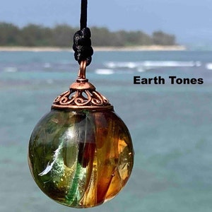Pode incluir: Um pingente esf&eacute;rico transparente com tons verdes e &acirc;mbar, suspenso por um cord&atilde;o preto. O pingente tem uma tampa decorativa cor de cobre. O texto "Earth Tones" &eacute; vis&iacute;vel na imagem.