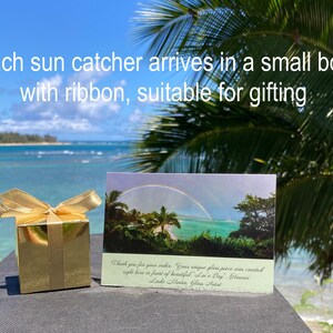 Pode incluir: Uma caixa de presente dourada com um la&ccedil;o de fita a condizer, um cart&atilde;o com um arco-&iacute;ris sobre o oceano e o texto "Each sun catcher arrives in a small box with ribbon, suitable for gifting."