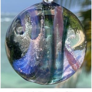 Pode incluir: Um globo de vidro transparente com redemoinhos turquesa e roxos, que lembram um c&eacute;u. O globo tem uma al&ccedil;a na parte superior para pendurar. O texto "Teal & Purple Sky" est&aacute; na parte inferior da imagem.