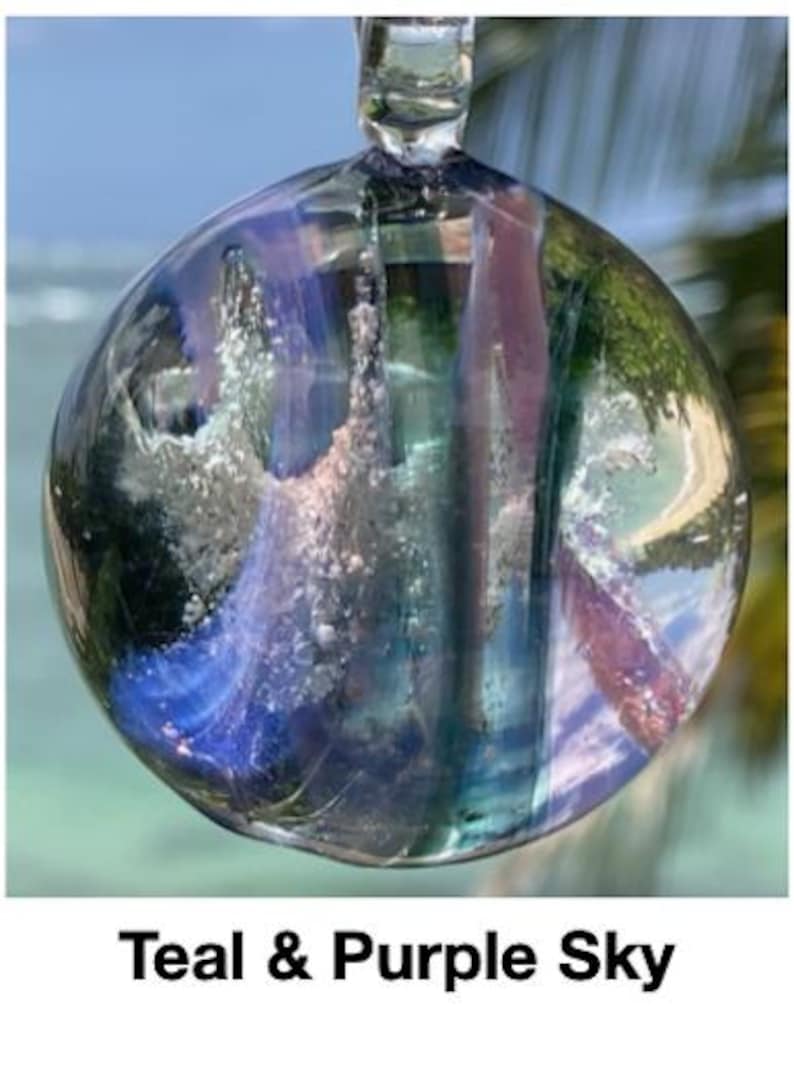 Pode incluir: Um globo de vidro transparente com redemoinhos turquesa e roxos, que lembram um c&eacute;u. O globo tem uma al&ccedil;a na parte superior para pendurar. O texto "Teal & Purple Sky" est&aacute; na parte inferior da imagem.