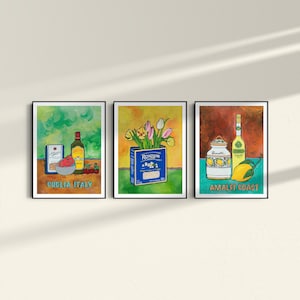 A triptych of colorful framed artworks on a light wall. The first shows Italian ingredients labeled Puglia, Italy. The middle depicts a Ronzoni pasta box with tulips. The third features limoncello and lemons labeled Amalfi Coast.
