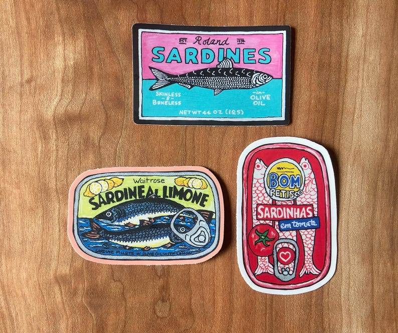 Puede incluir: Tres etiquetas de latas de sardinas de colores. La primera etiqueta es azul, rosa y blanca con el texto "Roland Sardines" y un dibujo de una sardina. La segunda etiqueta es rosa, amarilla y blanca con el texto "Waitrose Sardineal Limone" y un dibujo de dos sardinas. La tercera etiqueta es roja, blanca y amarilla con el texto "Bom Reitisco Sardinhas em tomate" y un dibujo de tres sardinas.