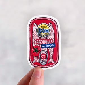 Puede incluir: Una pegatina de lata de sardinas roja y blanca con el texto "BOM PETISCO SARDINHAS em tomate" y un dibujo de sardinas y un tomate.