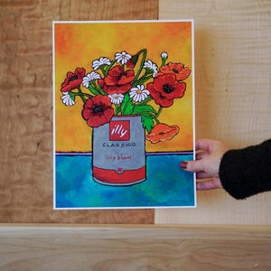Pu&ograve; includere: Un dipinto ad acquerello di un mazzo di papaveri rossi e margherite bianche in una lattina argentata con il logo Illy Classico Illy Blend. Lo sfondo &egrave; un gradiente di giallo, arancione e blu.