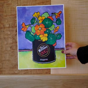 Puede incluir: Una pintura de un ramo colorido de flores naranjas y amarillas en una lata negra con el texto "Caffe Vergnano 1882" y "Roasted & Blended". El fondo es un degradado de morado y verde.