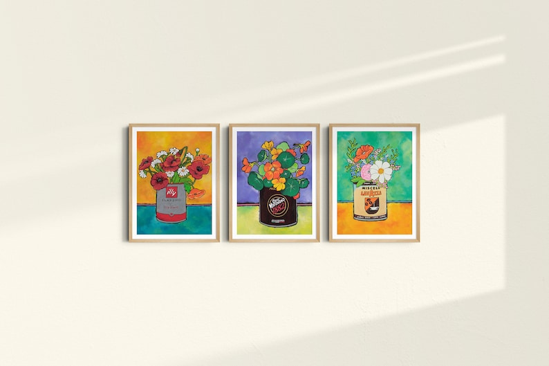 Pu&ograve; includere: Tre stampe incorniciate di composizioni floreali in lattine vintage. La prima stampa presenta fiori rossi in una lattina blu e rossa etichettata "Claussen Pickles". La seconda stampa presenta fiori arancioni in una lattina marrone etichettata "Wieners". La terza stampa presenta fiori rosa e bianchi in una lattina gialla e arancione etichettata "Miracle Whip Salad Dressing".