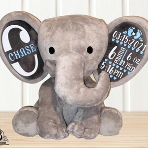 Puede incluir: Un elefante de peluche gris con orejas grandes. La oreja izquierda muestra el nombre "CHASE" en azul. La oreja derecha muestra detalles de nacimiento: 15/03/2021, 2,72 kg, 49,53 cm y 17:16, en azul. Un art&iacute;culo tem&aacute;tico para beb&eacute;s.