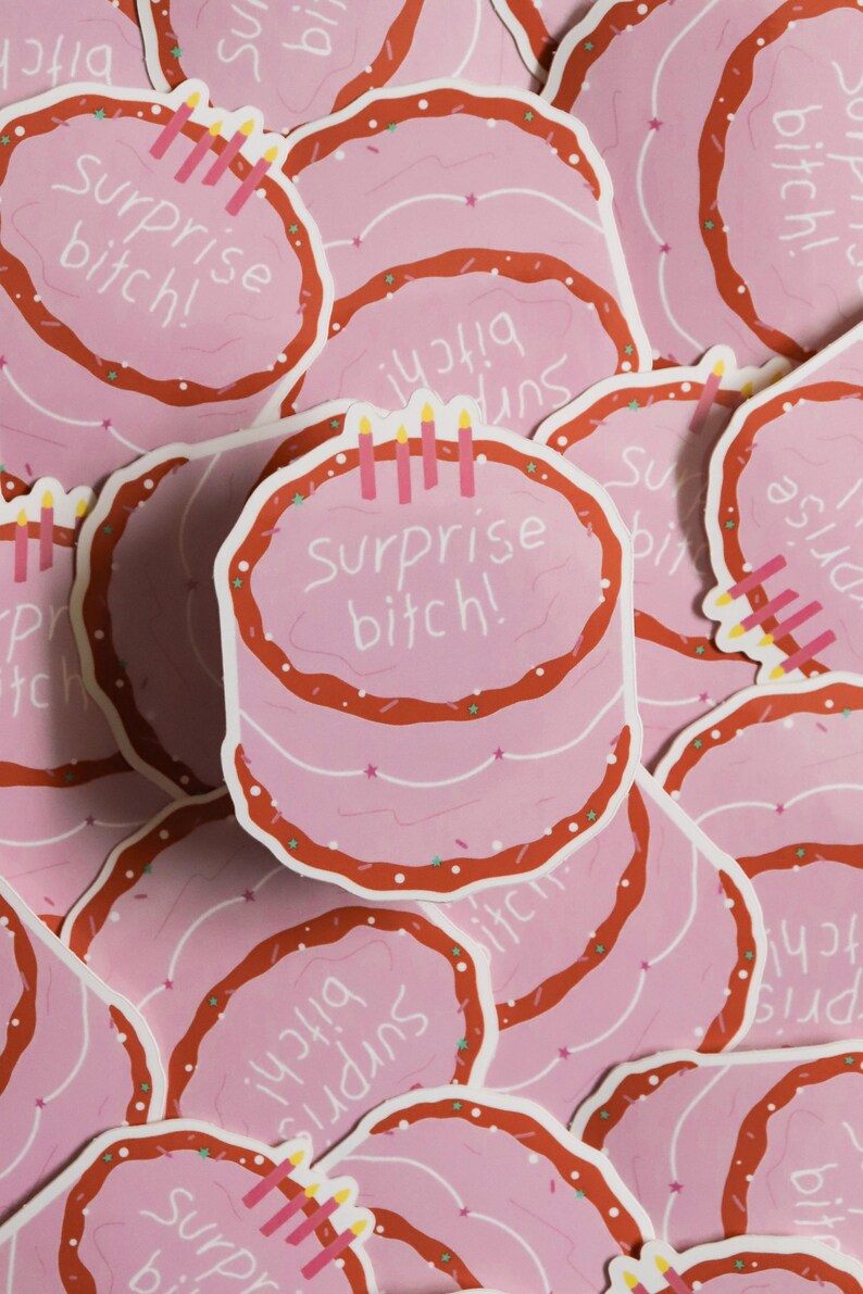 May include: Pink stickers featuring a cartoon cake design with red frosting and candles. The text "Surprise bitch!" is written on the cake. The stickers are scattered across the image.