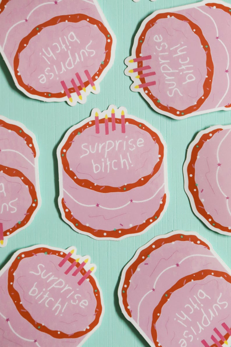 May include: Pink cake stickers with red frosting and the text "Surprise bitch!" are scattered on a light blue background. Each sticker has candles and sprinkles. The stickers are a fun, celebratory design.