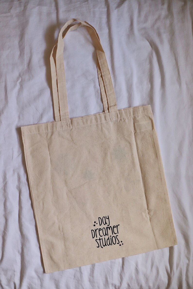 May include: A natural-colored tote bag with black handles and the text "..day dreamer studios.." printed on the front.