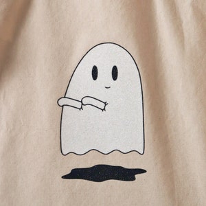 May include: A white tote bag with a glittery ghost design. The ghost is smiling and has its arms outstretched.