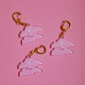 May include: Three pink and white cloud-shaped keychains with a gold chain and ring. Each keychain features a small cartoon person inside the clouds.