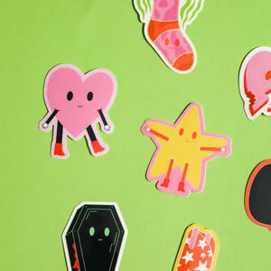 May include: A set of colorful stickers featuring a heart, a star, a boot, a sock, and a coffin. Each sticker has a cartoon face and is designed in a playful style.