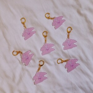 May include: Seven pink and purple cloud-shaped keychains with gold rings. Each keychain features a double-layered cloud with a star in the center.