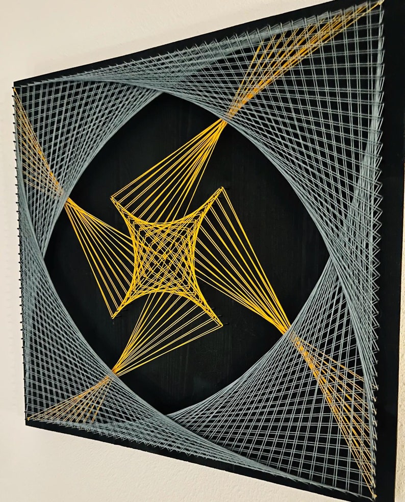 May include: A geometric string art piece with a black background and a design of intersecting lines in yellow and gray.