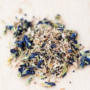 May include: A close-up of a blend of dried herbs and flowers for tea. The mixture includes blue butterfly pea flowers, lemongrass, and other herbs.