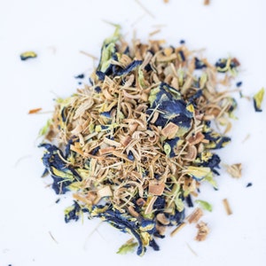 May include: A close-up of a blend of dried herbs and flowers for tea. The mix includes dried lemongrass, blue pea flowers, and other herbs.