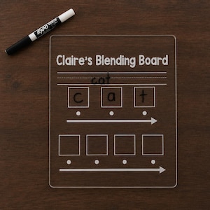May include: A clear acrylic rectangular blending board with the text Claire's Blending Board printed at the top. It features lines for writing, three boxes with the letters c, a, and t, and two rows of boxes with arrows. A black dry-erase marker is included.