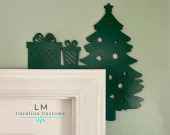 May include: Green wooden Christmas tree and gift decorations on a white door frame. The tree has a star on top and is decorated with circles and stars. The gifts are wrapped with polka dots and stripes. The door frame has the text "LM Carolina Customs" on it.